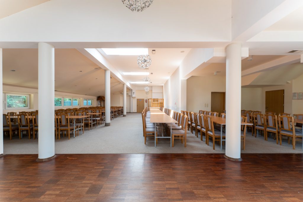 Sala konsumpcyjna z miejscem dla gości i układem stołów i krzeseł.
